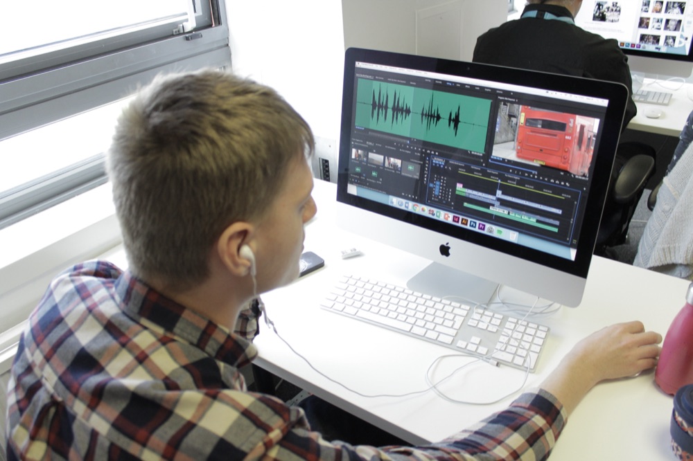 Individual editing audio in Adobe Premiere Pro on an iMac, Adobe Creative Cloud icons visible in the dock